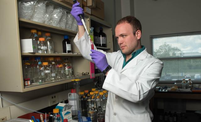 Man in lab coat putting fluid into a test tube.