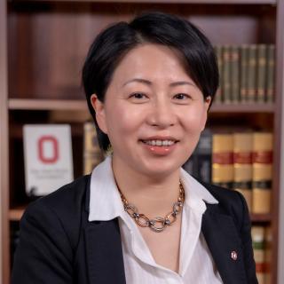 woman in dark suit sitting in front of bookshelp