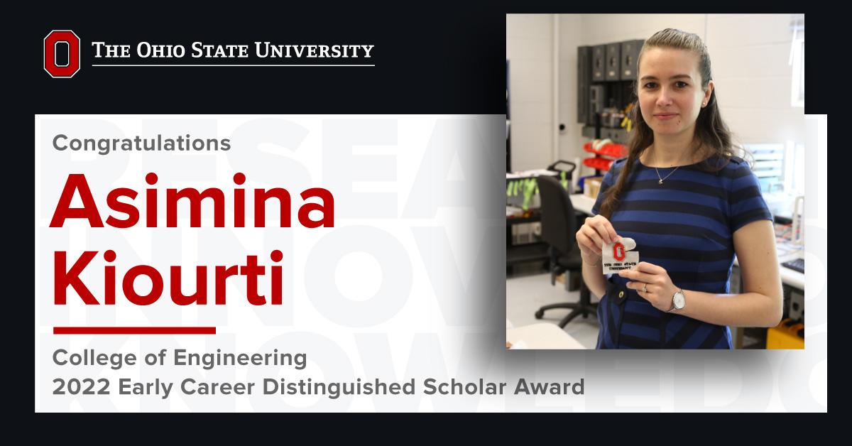 Asimina Kiourti in her lab holding an Ohio State patch smiling at camera