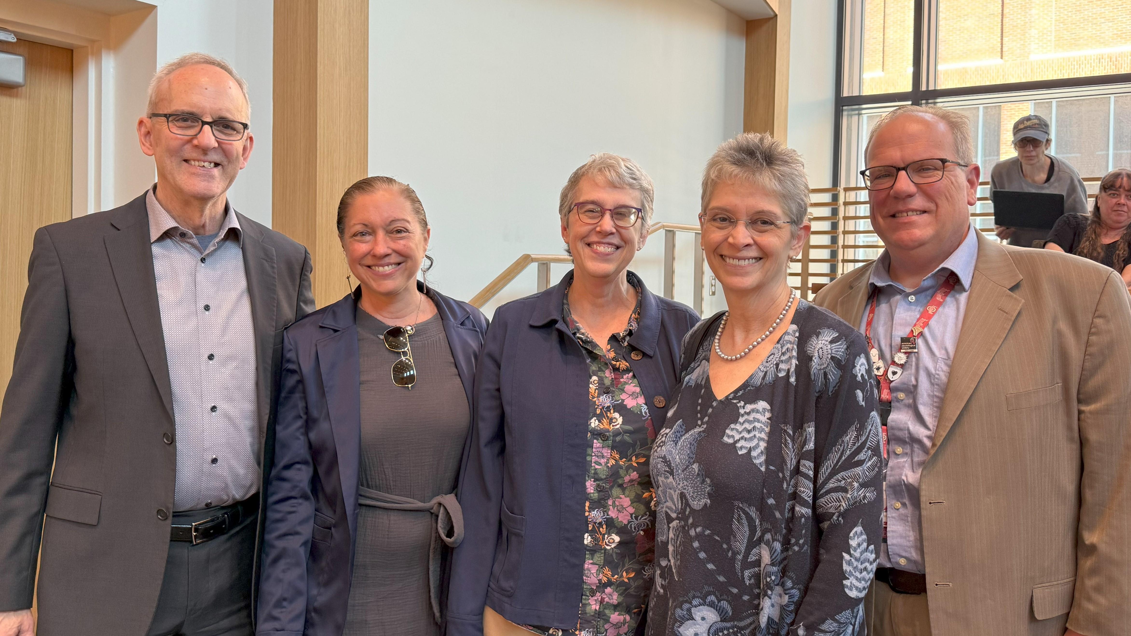 Five people pose before a group of people