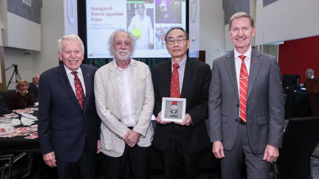 four men standing in a room with one holding an award medal